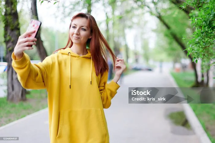 Một Cô Gái Xinh Đẹp Mặc Áo Hoodie Màu Vàng Chụp Ảnh Tự Sướng Cầm Điện Thoại  Trong Tay Và Điều Chỉnh Tóc Hình ảnh Sẵn có - Tải xuống Hình ảnh