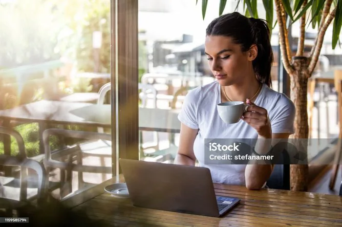 Cô Gái Trẻ Xinh Đẹp Ngồi Ở Bàn Trong Quán Cà Phê Bên Cửa Sổ Uống Cà Phê  Cappuccino Người Phụ Nữ Xinh Đẹp Làm Việc Với Máy Tính Xách Tay Từ